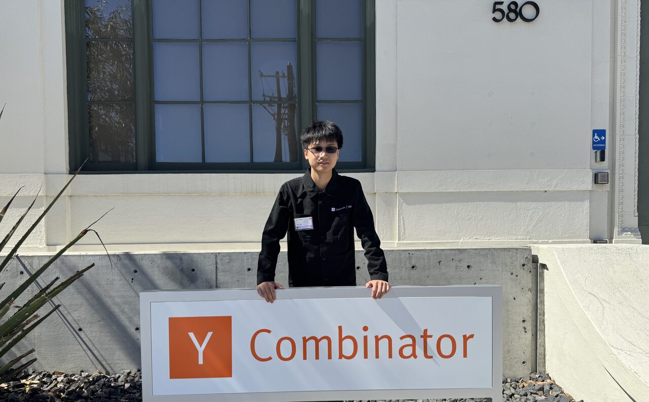 Jeremy Huang standing behind the Y Combinator sign at 580, wearing a YC badge